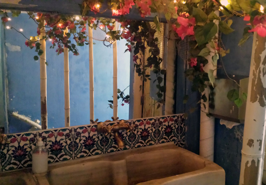 VIVA LA VIDA-baño del restaurante vegetariano con una gran pila de piedra, adornado con flores y guirnaldas de luces